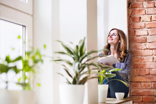 Woman sitting at home on the window sill, reading a book