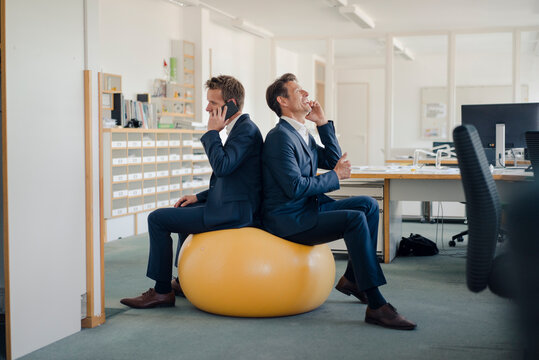 Two businessman checking smartphone with yellow fitness  ball in foreground