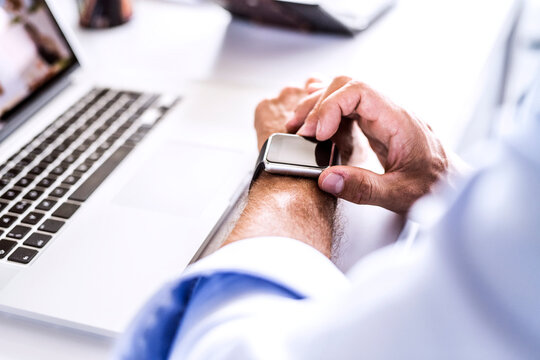 Close-up of businessman at desk with laptop using smartwatch