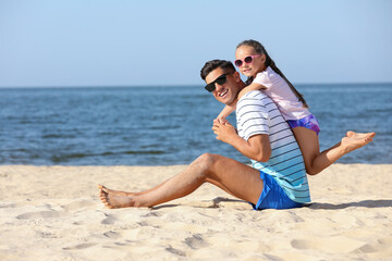 Fototapeta premium Father and daughter on sandy beach near sea. Summer holidays with family