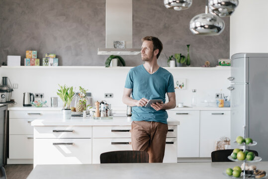 Man with tablet standing in the kitchen looking at distance