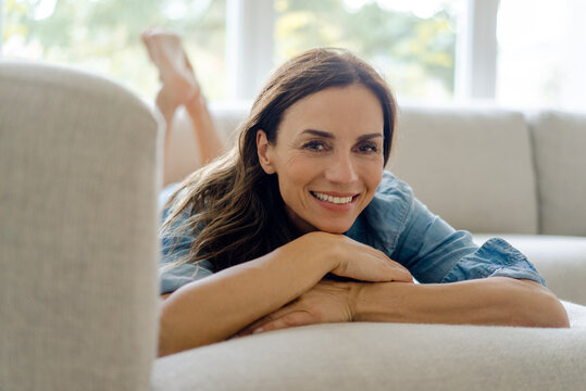 Portrait of smiling mature woman lying on couch at home