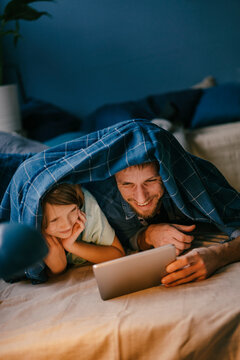 Happy father and son watching a movie on tablet under blanket