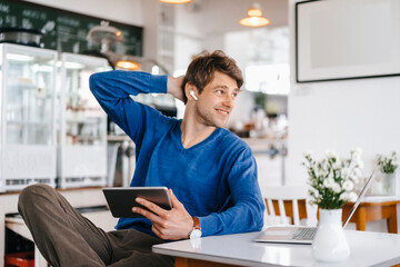 Smiling man in a cafe with earphone, laptop and tablet