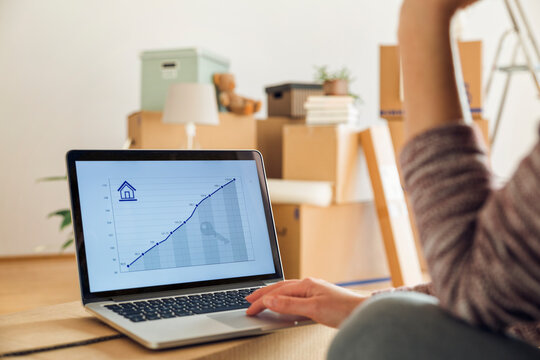 Woman using laptop with rising line graph on the screen in a new home