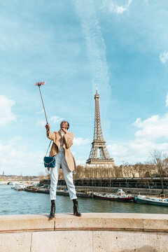 France, Paris, Woman standing on bridge over the river Seine with the Eiffel tower in the background taking a selfie