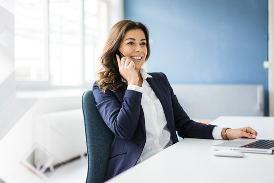 Portrait of smiling businesswoman on the phone sitting at desk in an office