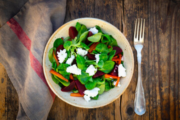 Bowl of vegetarian salad with roasted carrot strips, beetroot, corn salad, goat cheese and Spanish onions
