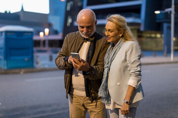 Spain, Barcelona, senior couple sharing cell phone in the city at dusk