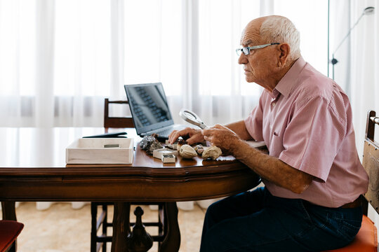 Retired senior man using magnifying glass for research of fossil and mineral at home