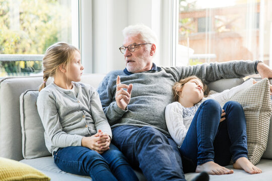 Grandfather talking to two girls on sofa in living room
