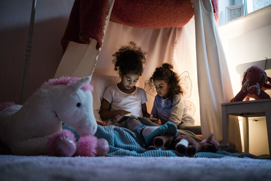 Two sisters sitting in dark children's room, looking at digital tablet