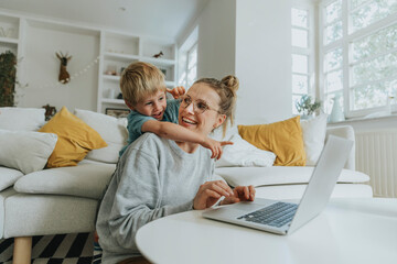 Boy pointing at laptop while standing behind mother at home