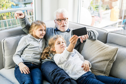 Two girls and grandfather on sofa taking a selfie