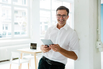 Portrait of happy businessman with tablet in bright office