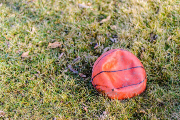 Deflated dirty orange basketball on grass.