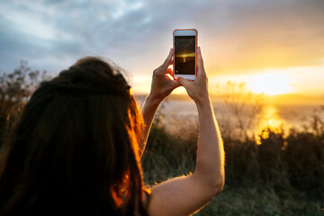 Young woman photographing sunset sky through smart phone