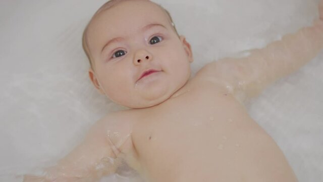 A nice little caucasian newborn baby is funny smiling, lying at the back in the bath. Portrait of a playful and energetic child close-up.