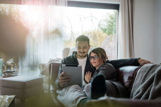 Smiling couple lying on couch at home sharing tablet