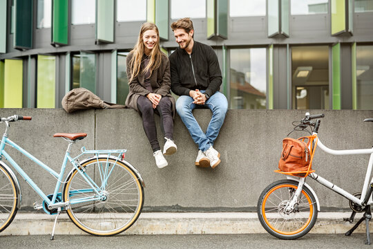 Happy couple with bicycles sitting on a wall