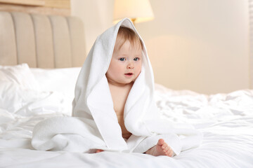 Cute little baby with soft towel on bed after bath