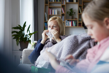 Mother sitting on couch, having a cold, daughter playing in foreground