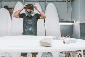 Mature man wearing protective face mask while shaping surfboard