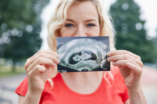 Portrait of happy pregnant woman holding ultrasound image outdoors