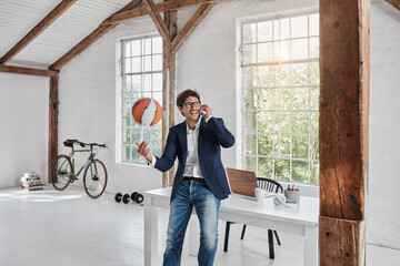 Laughing businessman with basketball on cell phone in penthouse
