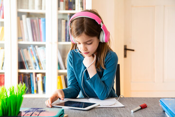 Little girl doing homework with headphones and digital tablet