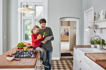 Smiling father and daughter with bell pepper and tablet in kitchen