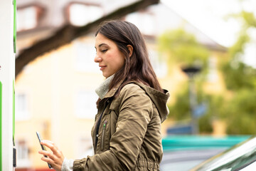 Beautiful woman using smart phone for renting electric car at charging station