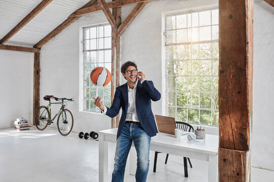 Laughing businessman with basketball on cell phone in penthouse