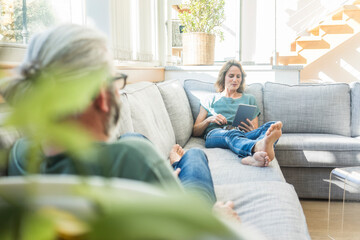 Mature couple relaxing on couch at home with woman holding tablet