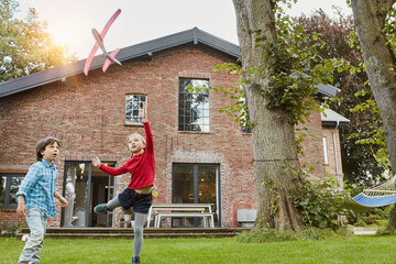 Two children playing with toy airplane in garden of their home