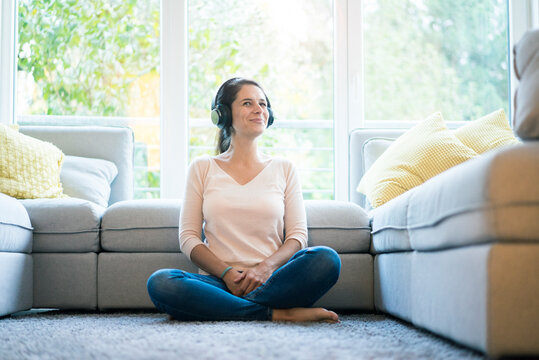Woman sitting alone on couch, listening music with headphones