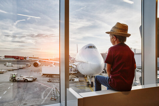 Boy wearing straw hat looking through window to airplane on the apron