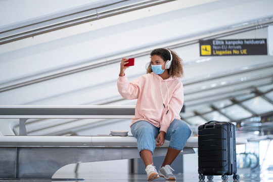 Young woman taking selfie while listening music through headphone at airport
