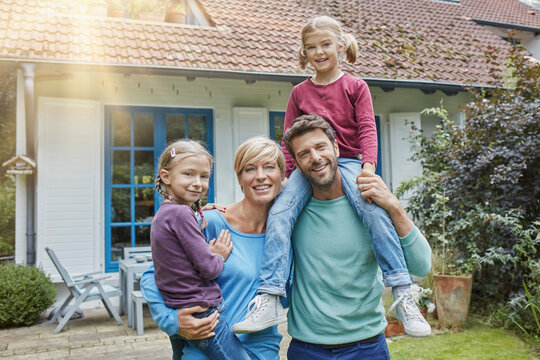 Portrait of happy family with two kids in front of their home