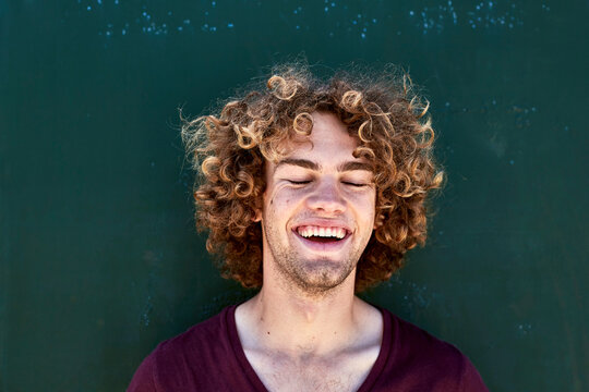 Portrait of laughing young man with curly hair in front of a green wall