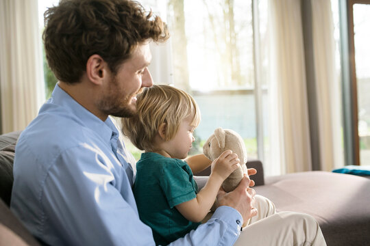 Father and son playing with teddy bear on couch at home