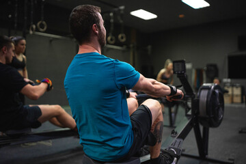 Man using rowing machine with people exercising in background at gym