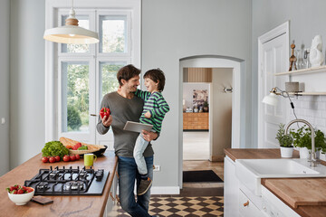 Happy father and son with bell pepper and tablet in kitchen