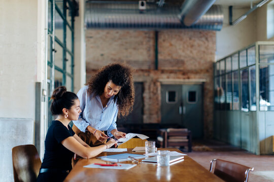 Two young businesswomen talking at conference table in loft office