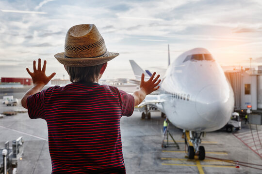 Boy wearing straw hat looking through window to airplane on the apron