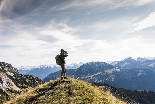 Austria, Tyrol, young man standing in mountainscape looking at view with binoculars