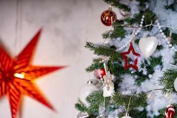 Decorated Christmas tree in the room. Coniferous tree with white and red baubles located near the white wall during the celebration of the holiday