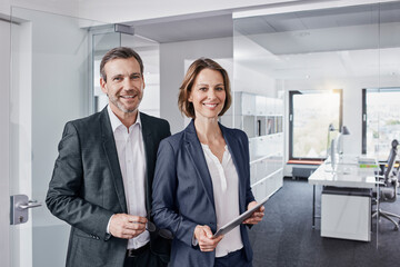 Portrait of smiling businessman and businesswoman with tablet in office