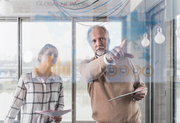 Casual mature businessman and young woman discussing data at glass pane in office