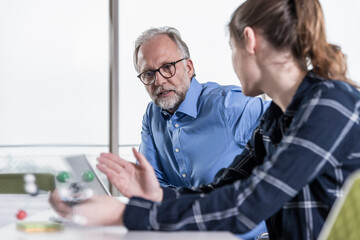 Mature businessman and young woman with atomic model talking in conference room